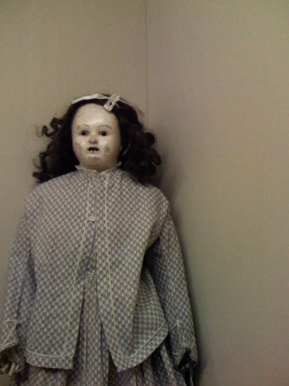 an old doll with black hair and eyes is posed on a shelf