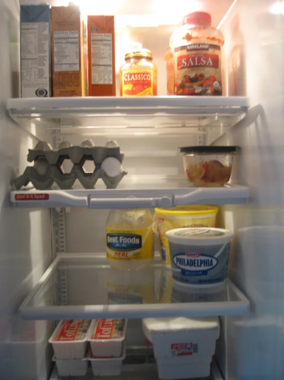 an opened refrigerator with eggs, milk, and various toppings