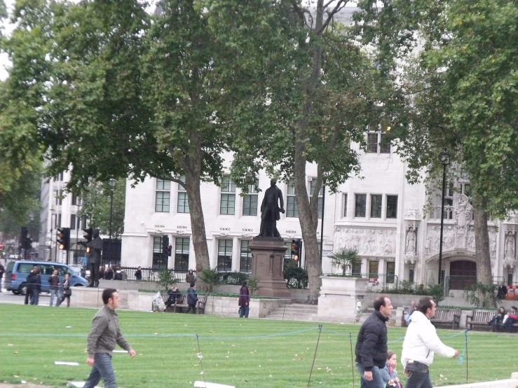 there are people walking along the park while looking at the statue