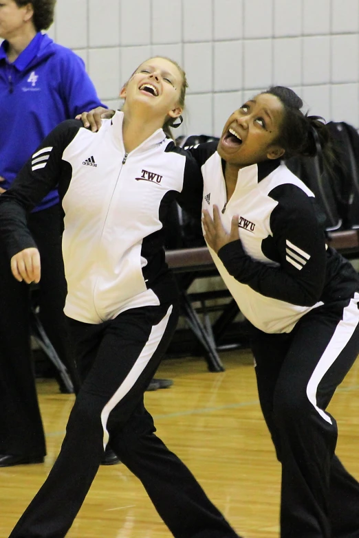 two young women dressed in black and white, dance together on a gym floor