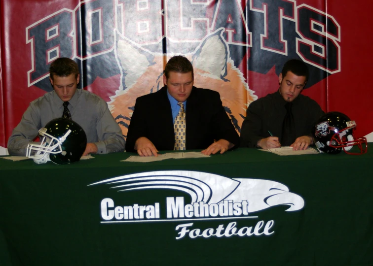 three men signing a paper sign in front of a large wall