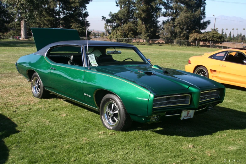 a car with hood on it is parked in the grass next to a yellow sports car