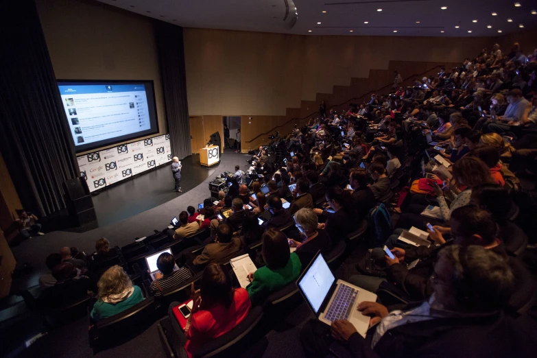 rows of laptops on tables as people are sitting in auditorium seats