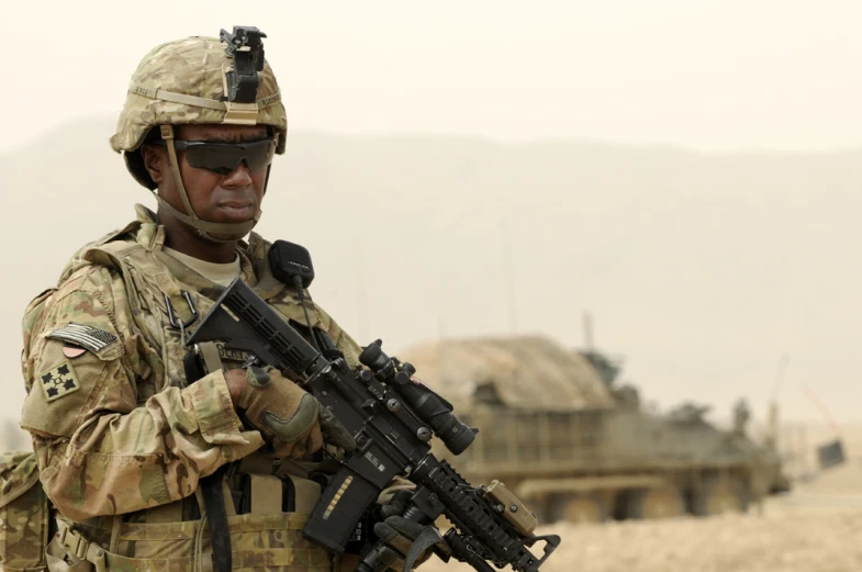 a man in camouflage with a gun standing next to a armored vehicle