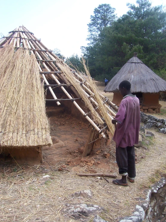 a person standing near an adobe hut built of sticks