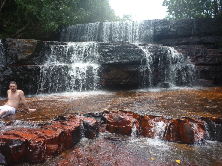 a man sitting next to waterfall in the jungle