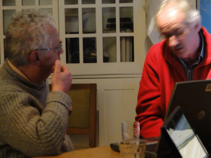 an old man and older man sitting together having a conversation while looking at a laptop computer