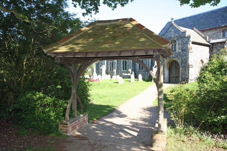 a wooden gazebo near some bushes and a stone building