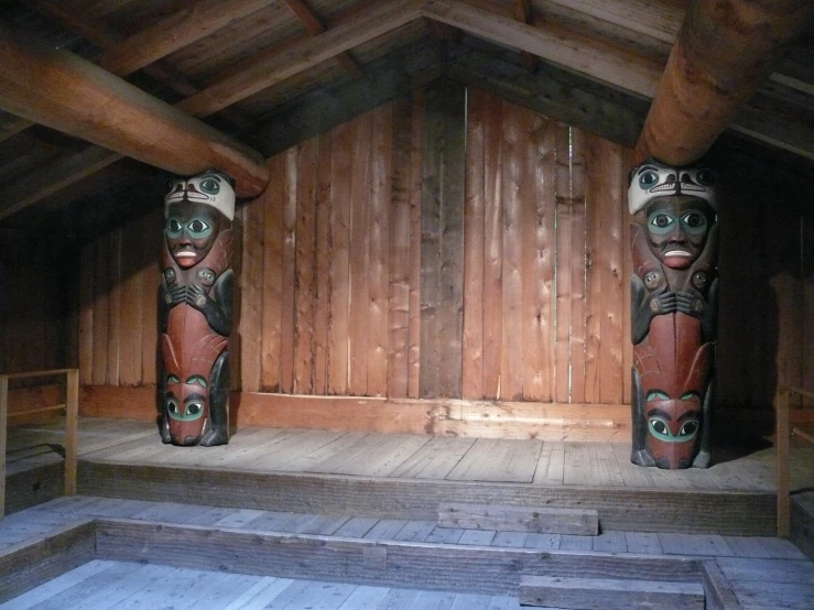 two carved totemas in a wooden room with stairs