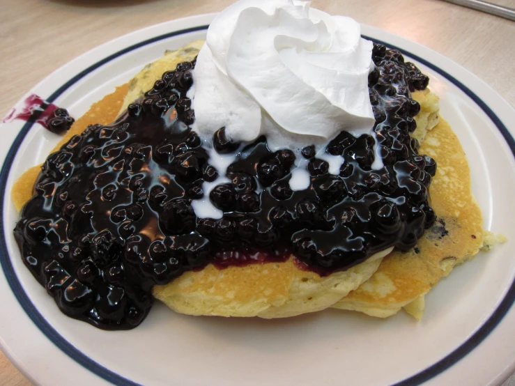 a plate has pancakes with blueberries and whip cream on it