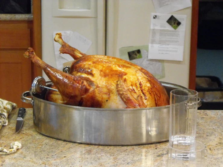 a whole turkey sits in a pot next to two glasses on the counter