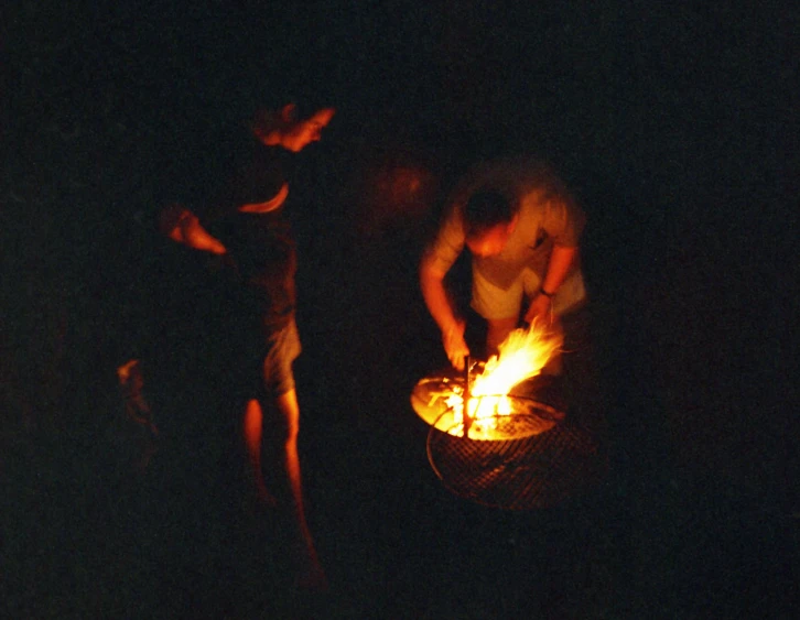 people stand around a fire pit and light it