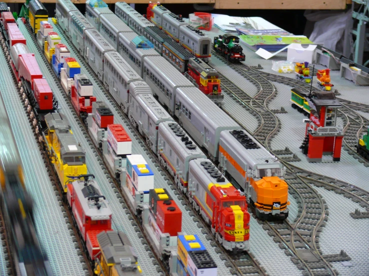 many toy trains are on the tracks with a building in the back