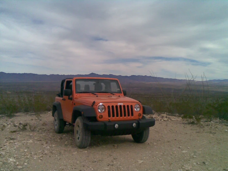 an orange truck on a dirt road with mountains in the background