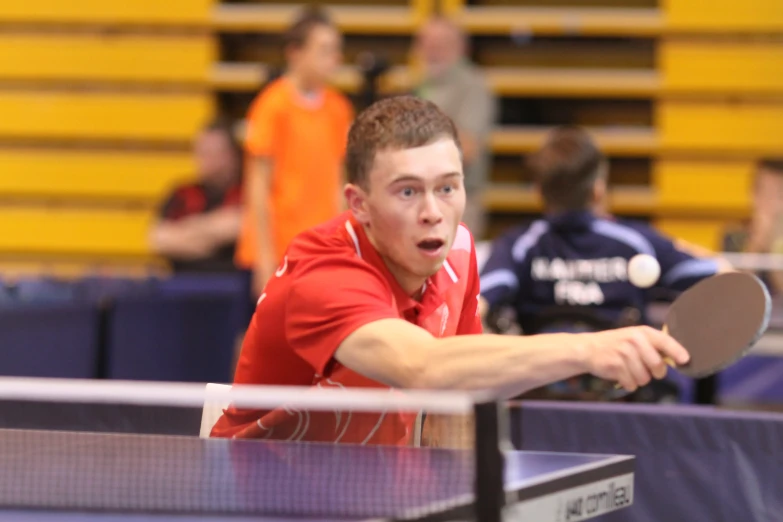 a young man holding a ping pong paddle at a ping pong game