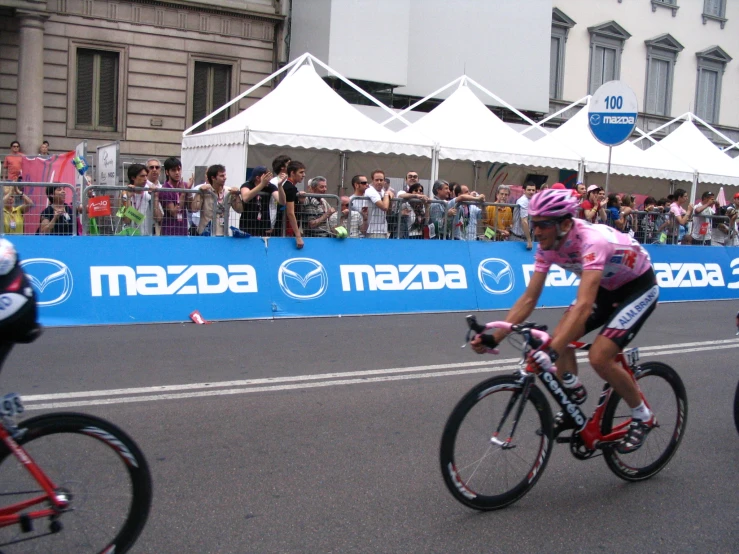 people riding bicycles on a race track while people watch from the street