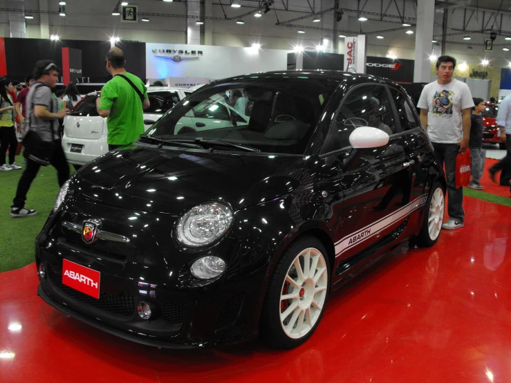 people walk by a compact car at an indoor auto show