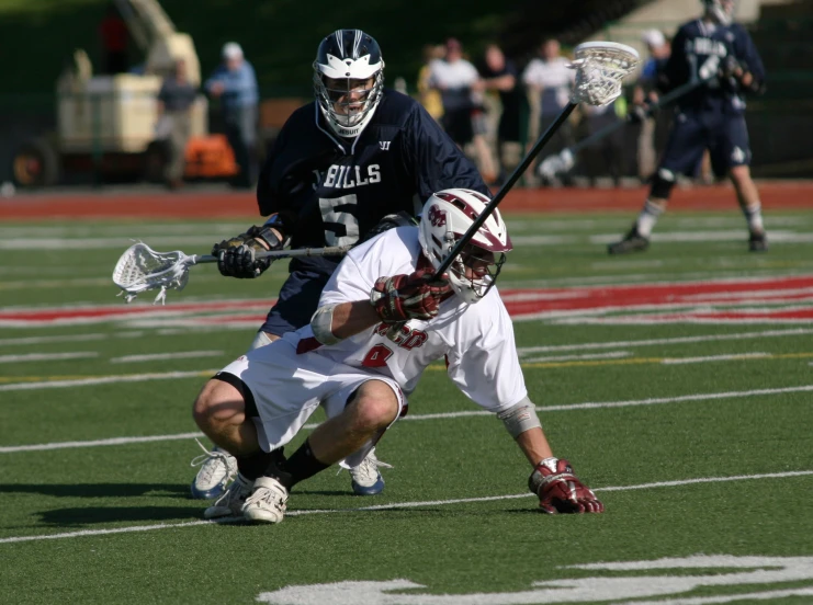 two boys wearing uniforms playing lacrosse on field