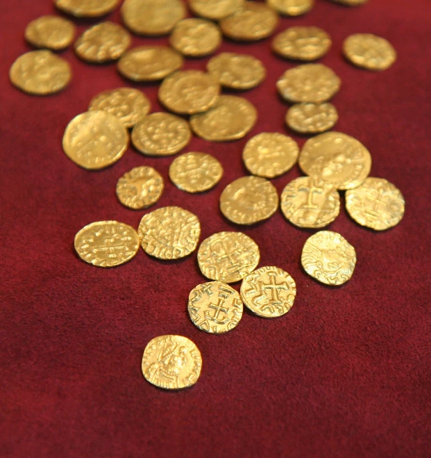 a pile of old gold coins scattered over a red table