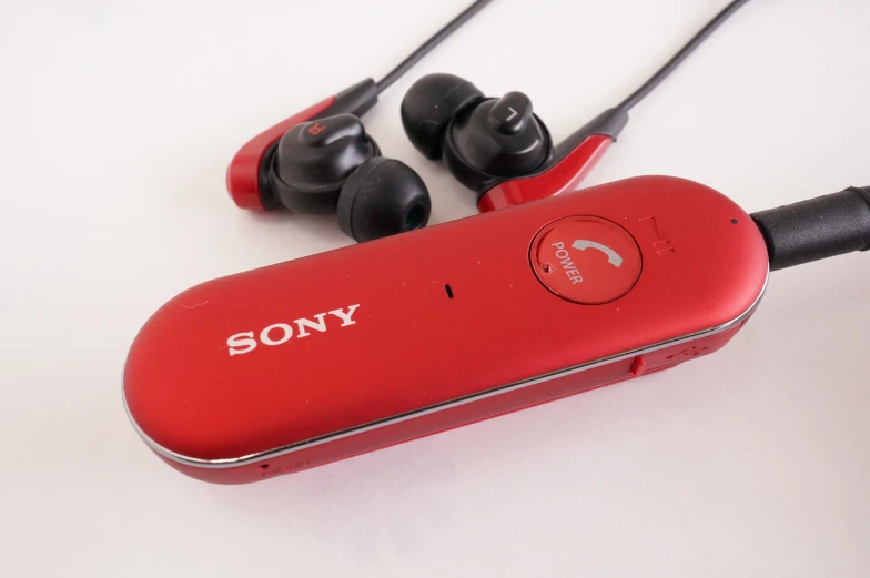 a red sony headphone sits on the table next to ear buds