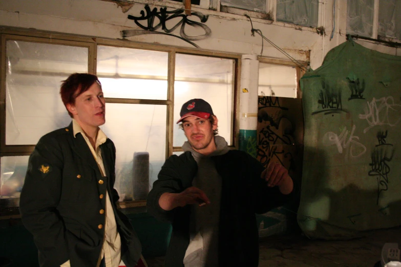 two young men standing in a run down building looking at soing on the side