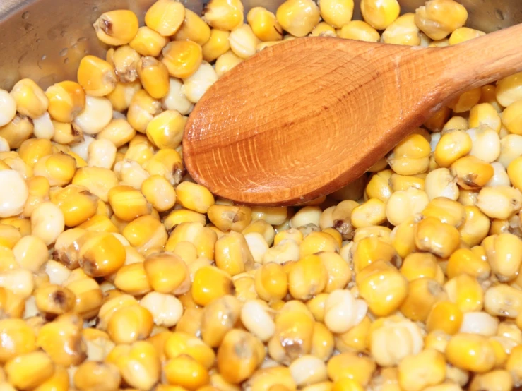 a wooden spoon is stirring a pot with some corn