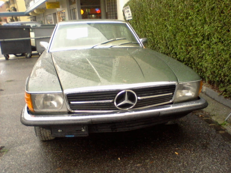 an old and shiny mercedes car parked in front of a fenced off building