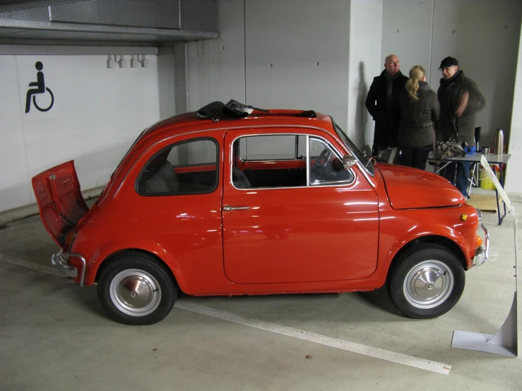 people in a garage are talking and others are standing around the car