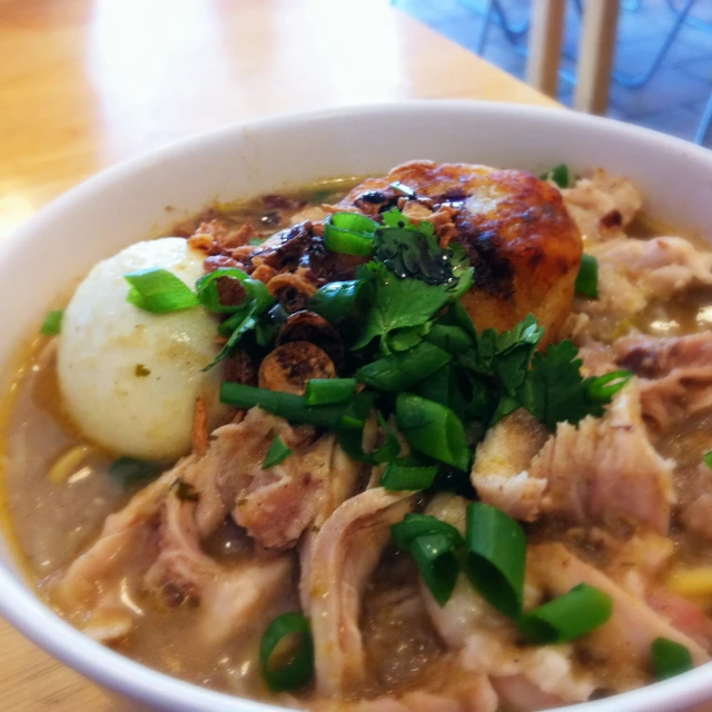 a bowl of food with green onions and meat on the side