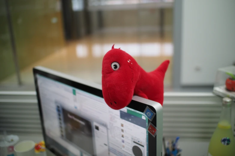 a red stuffed animal sitting on the back of a laptop