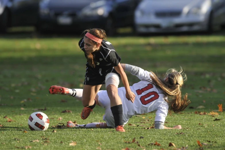 two girls in the grass, one is playing soccer while one girl lays on the ground