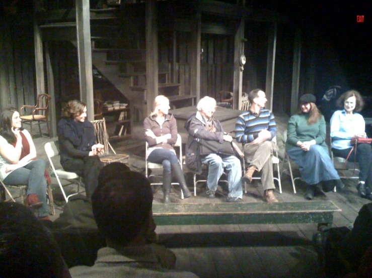 several people sitting in chairs at a stage while another person stands at the end