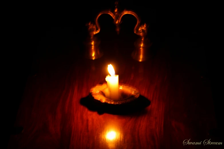 a lit candle on a wooden table in the dark