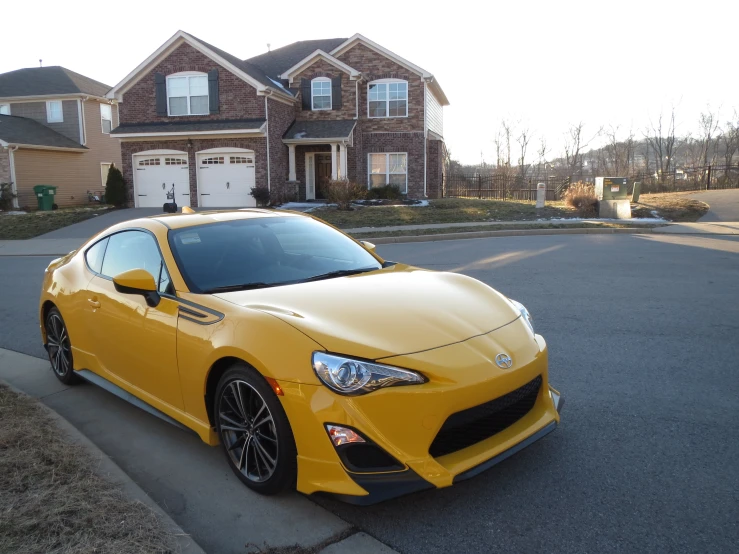 a yellow sports car sitting in front of a brown house