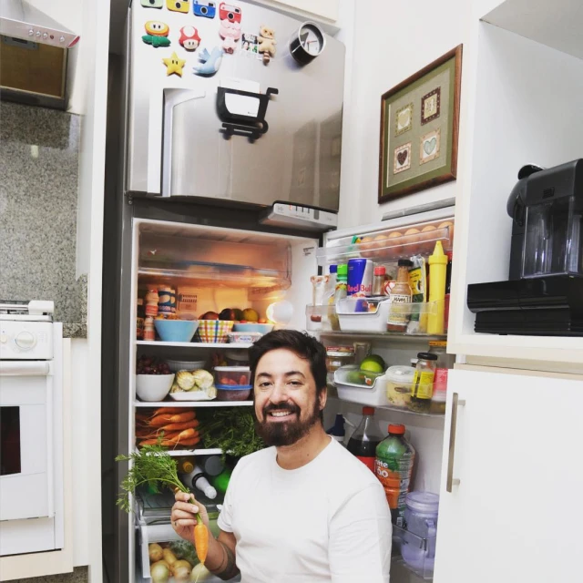 a man is holding a carrot inside of his refrigerator