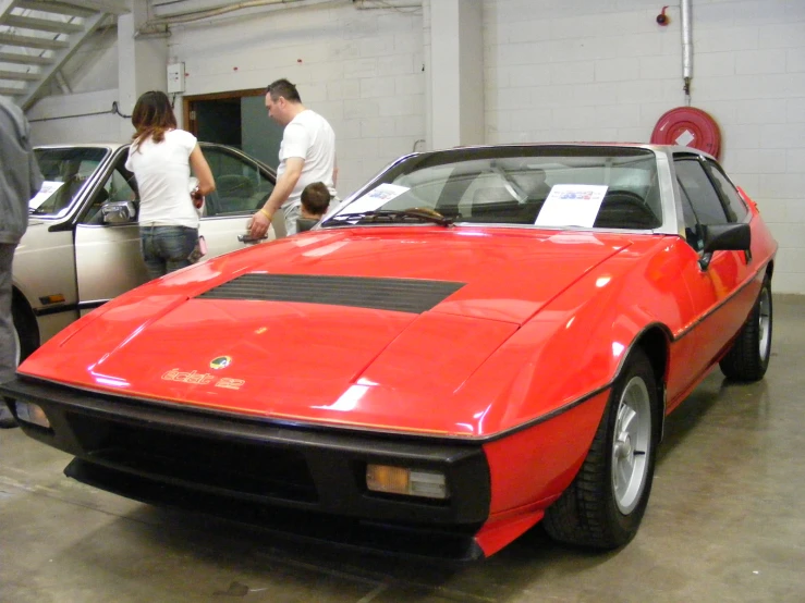 group of people standing around a red car in a garage