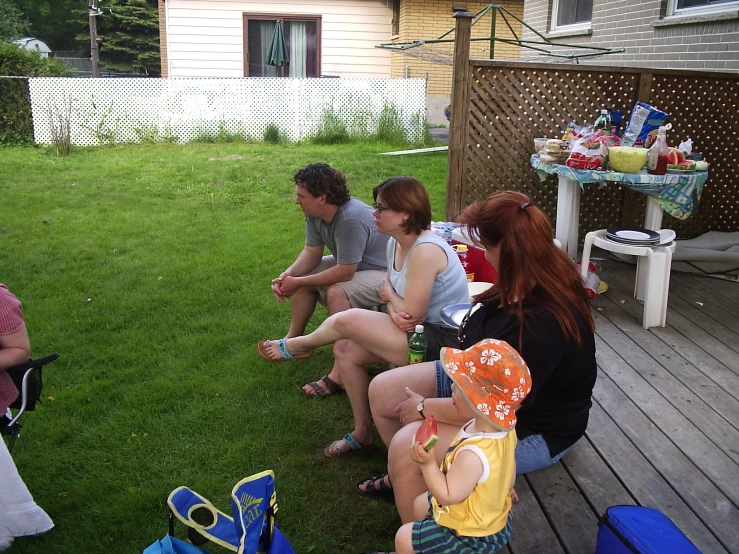 people sit outside in the grass, talking and eating