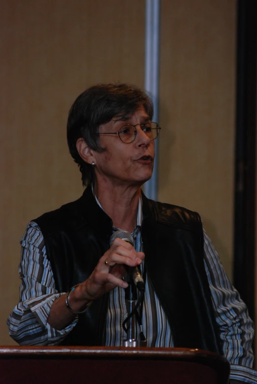 a woman at a podium wearing glasses holding a microphone