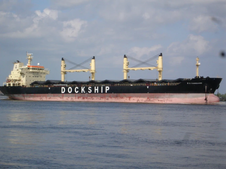 a black and red container ship floating next to an island
