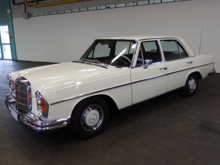 an old car sits in a large white garage