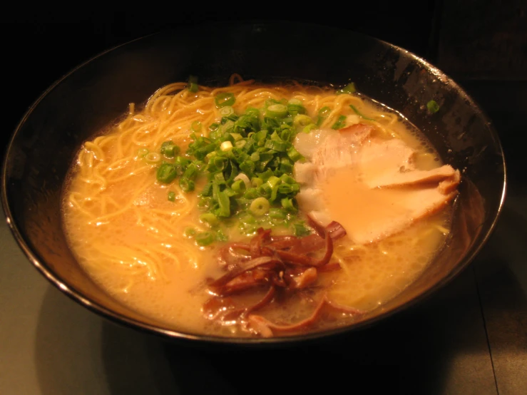 the bowl contains noodles and ham broth, green onions and green onions