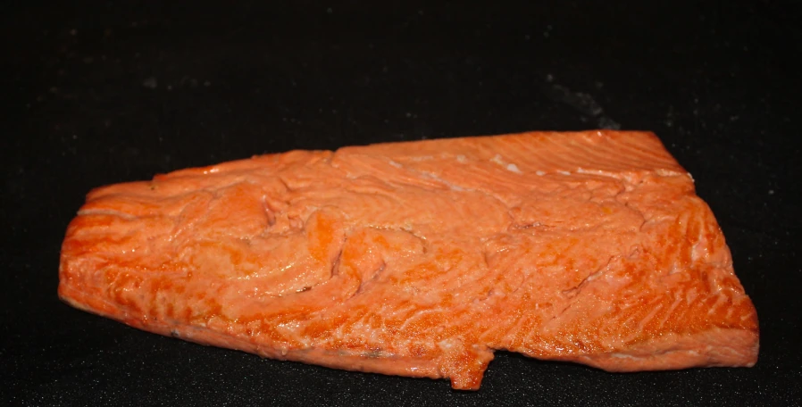 a piece of raw salmon sitting on top of a black surface