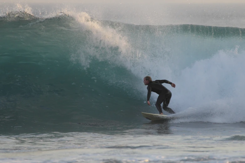 a surfer in black wet suit rides large waves on a surfboard