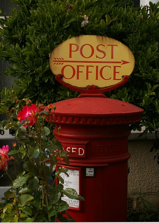 a red post office mail box next to some plants