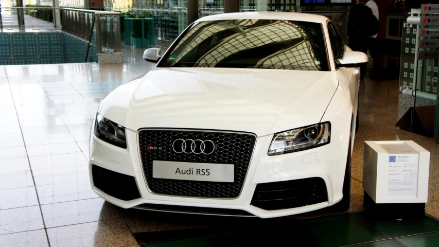 the front end of a white audi car parked inside of a building