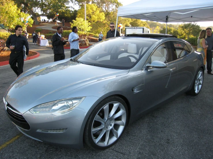 a silver car on road next to people