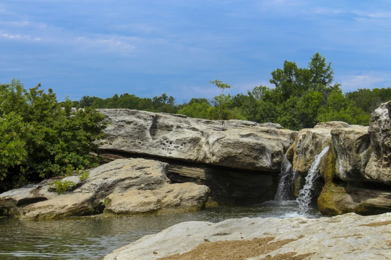 some rocks and bushes are around a water fall