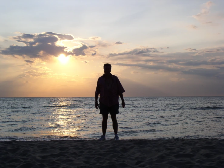 a man is standing on the beach and watching the sun rise