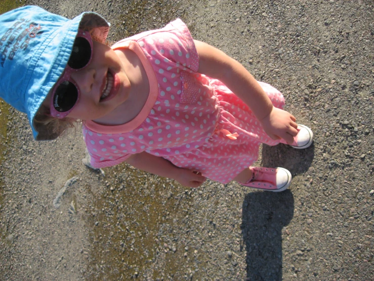 a little girl standing in the dirt on top of a skateboard