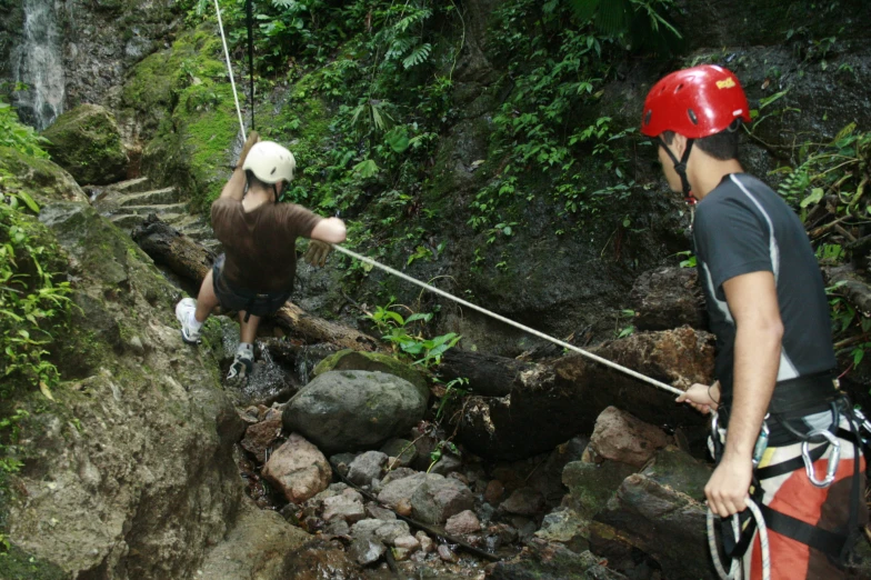 man in climbing gear holding onto a rock with another man near by